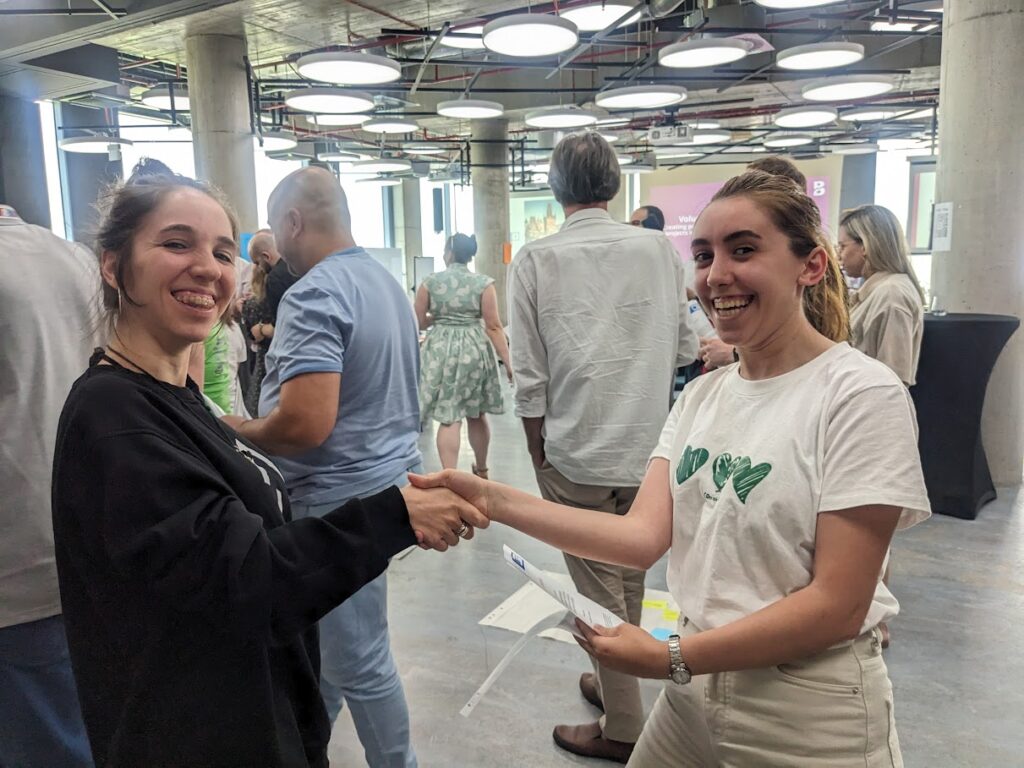 two girls in a busy seminar room congratulating each other shaking hands and smiling