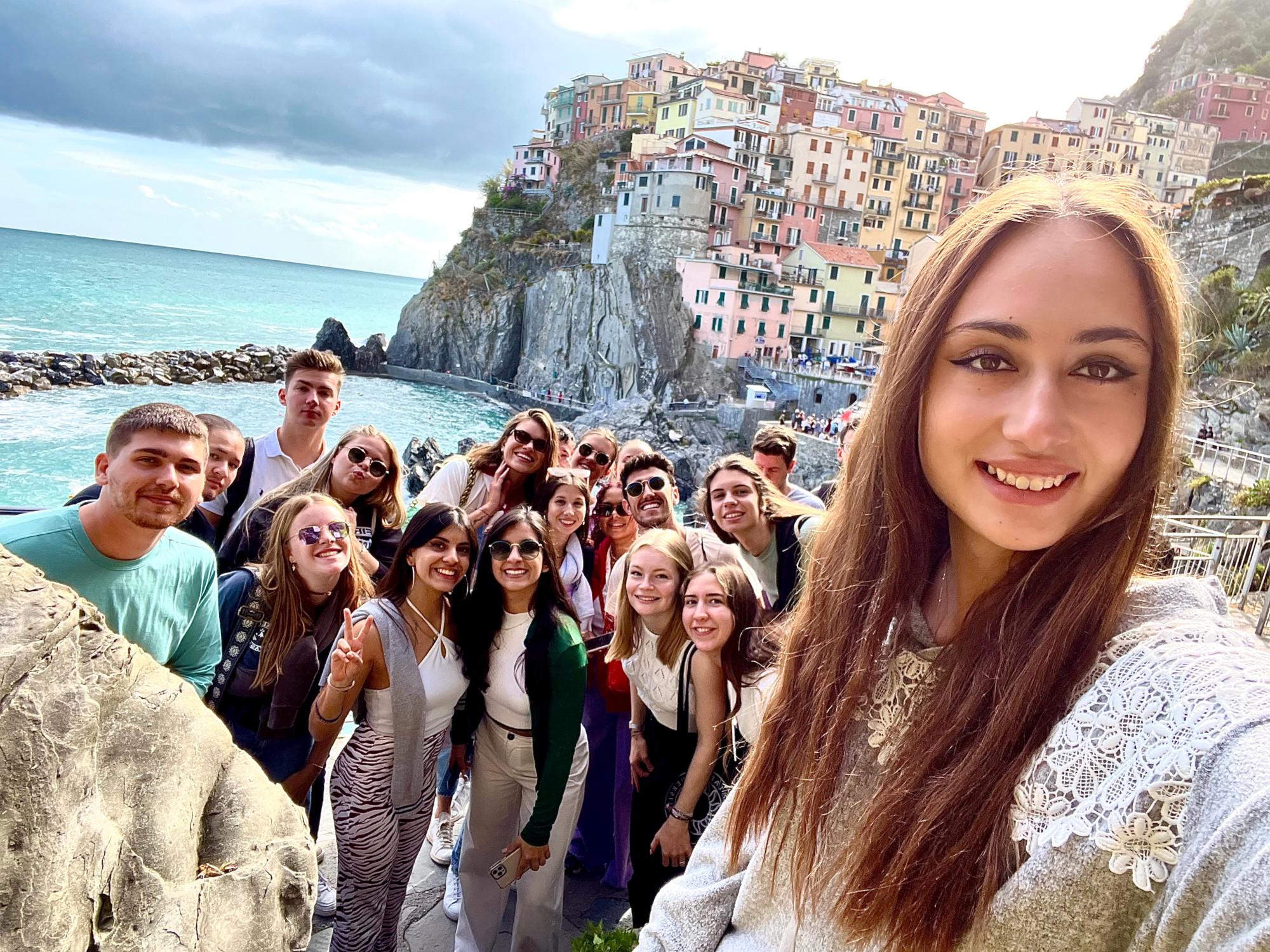 A young girl with a group of other young adults with an old Italian town on a rocky cliff and a sea down