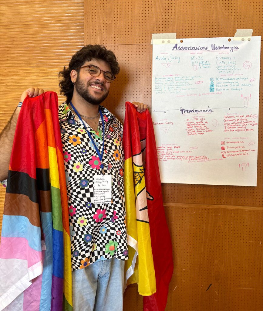 A young men in colourful shirt with flags in hands and a hand-written poster behind