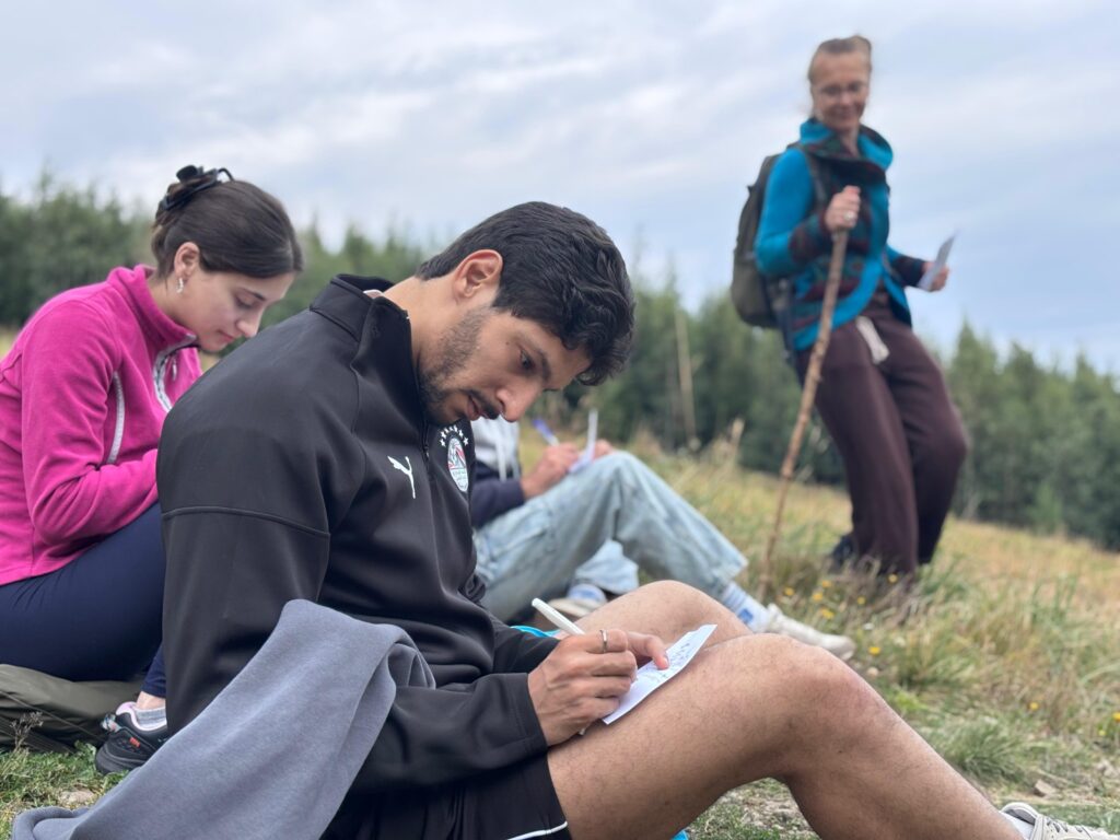 Young man and woman on the mountain meadow, sitting and writing notes